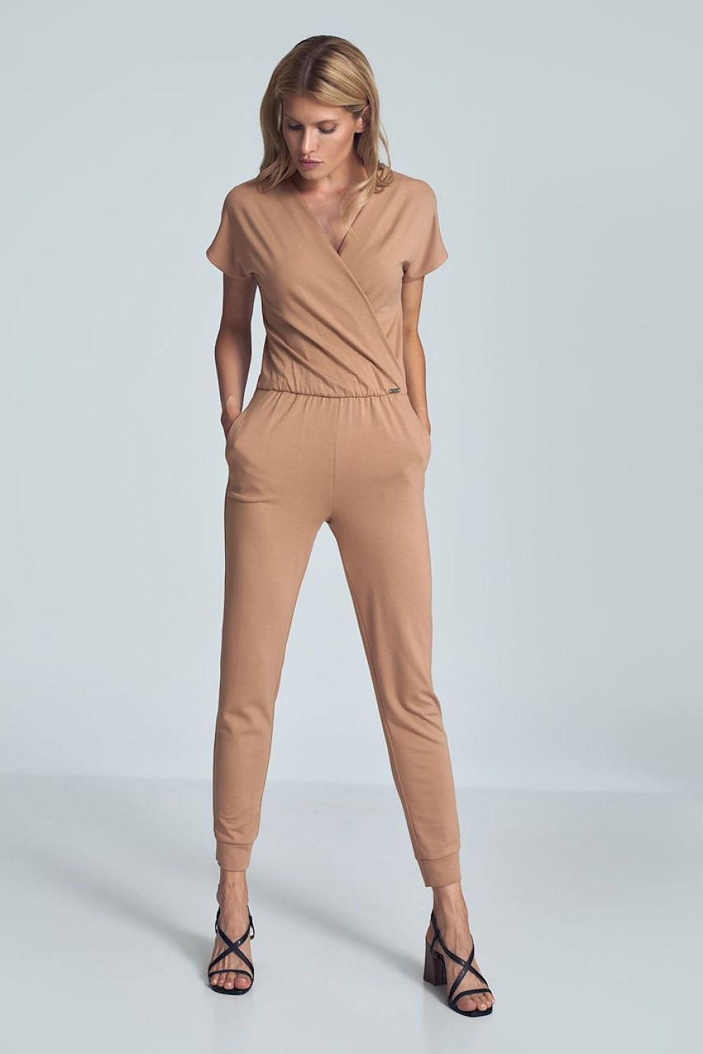 Beige jumpsuit met crinkle halslijn, elastische taille en taps toelopende pijpen met drawstring.